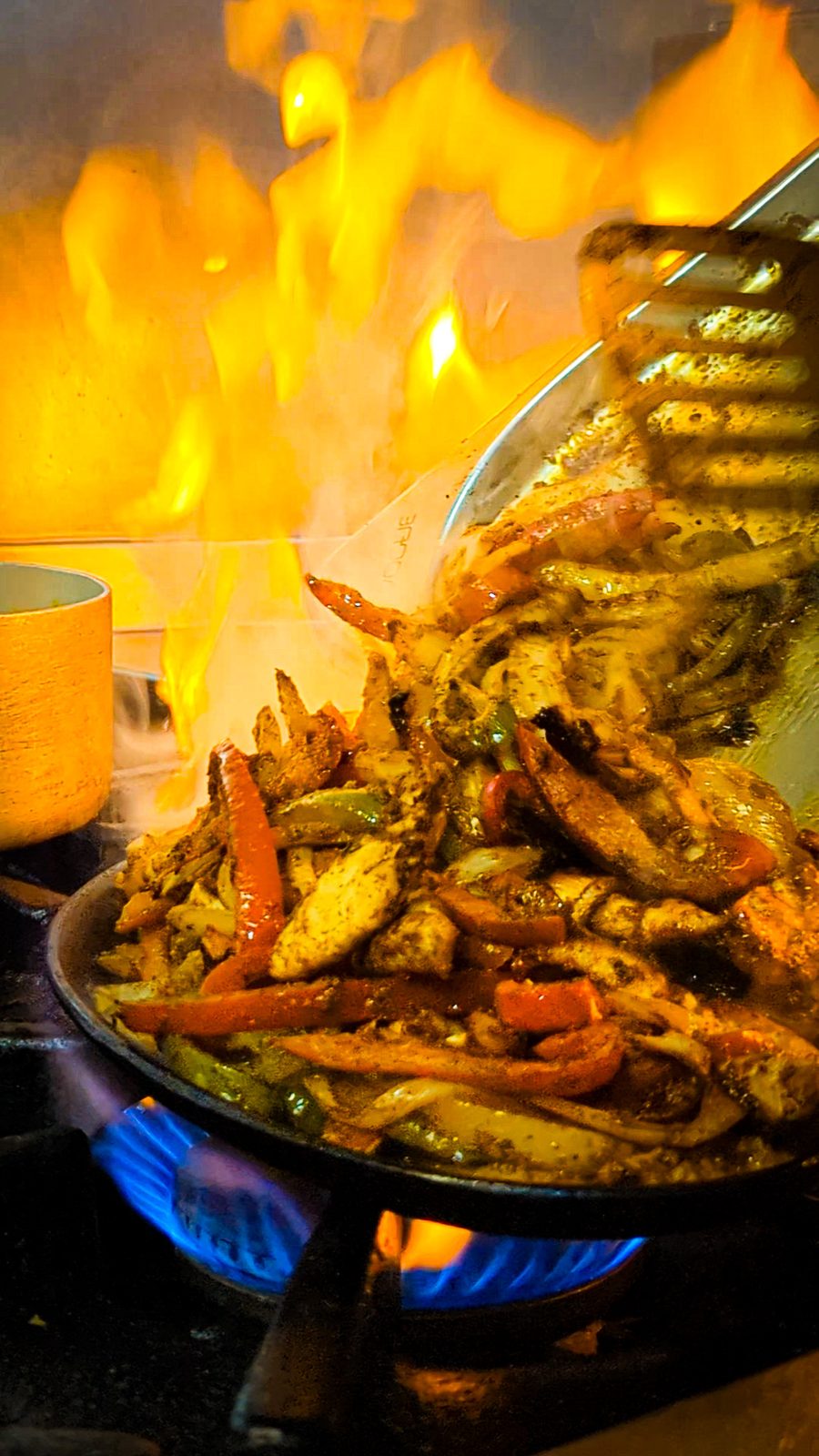 A pan of food on the stove with flames climbing the wall behind
