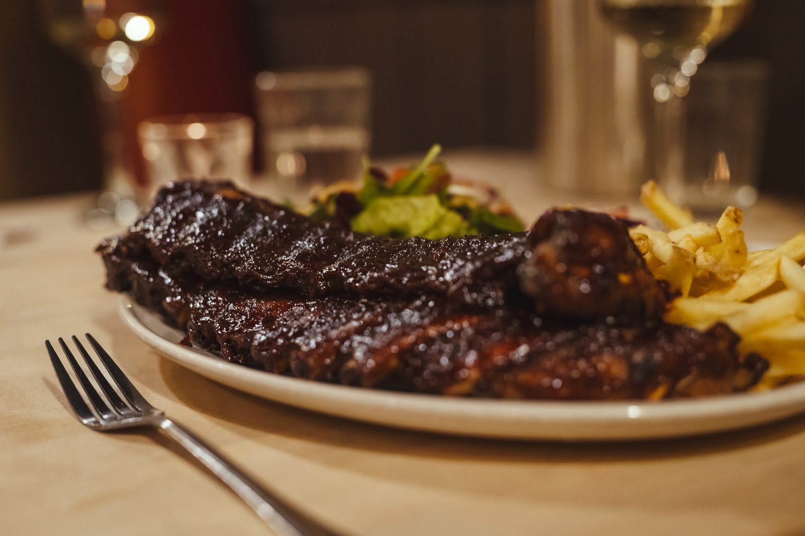 A plate of glazed ribs and chips by candlelight